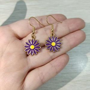 Detalle de pendientes de margarita en esmalte púrpura con ganchos dorados y centro amarillo