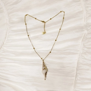 Macro detail of conch shell pendant on a gold beaded chain with lobster clasp closure