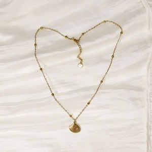 Detailed view of gold shell pendant necklace with small gold beads on white silk fabric