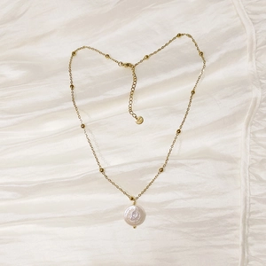 Macro detail of gold stainless steel bead chain and white embossed crown coin pendant