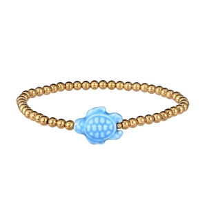 Close-up of gold beaded bracelet featuring a light blue ceramic sea turtle charm