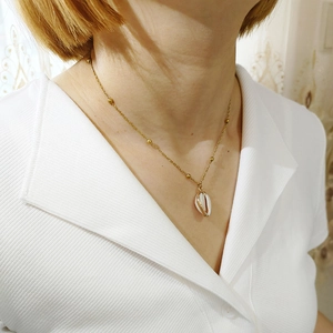 Close-up of a bohemian gold bead necklace featuring a natural white cowrie shell pendant