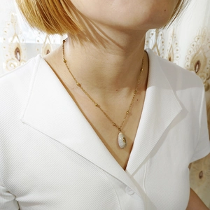 Detail of bohemian gold bead chain necklace with natural seashell pendant on model