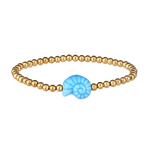 Macro detail of a waterproof gold bead bracelet with a blue ceramic conch charm