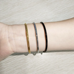 Close-up of minimalist gold, silver, and black stainless steel bangles with polished finish