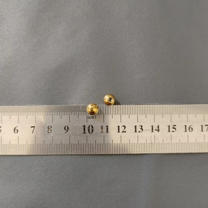 Detail view of 4mm golden stainless steel beads measured with a ruler on a textured surface