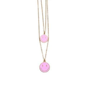 Dettaglio di collana dorata a due strati con ciondoli smiley in smalto rosa su sfondo bianco