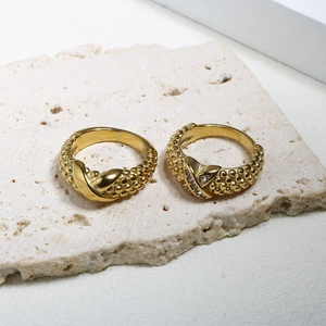 Goldene X-förmige Ringe mit Zirkonia-Akzenten auf beigem Steinhintergrund