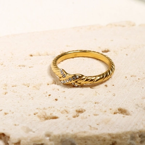 Detail eines goldenen gedrehten Rings mit Pavé-Unendlichkeitsknoten auf beigem Stein