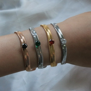 Close-up of flat snake chain bracelets with colorful crystal center stones in multi-tone metal