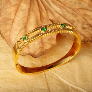 Vintage gold-plated titanium steel cuff bracelet with green zircon stones on dry leaves