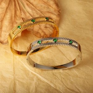 Detailed view of hollow gold and silver bracelets set with round emerald green zircon gems