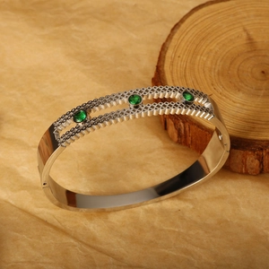Silver stainless steel bangle with green zircons and hollow textures on a rustic background