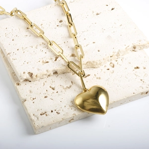 Close-up of a 18k gold plated paperclip chain with a polished heart pendant on travertine