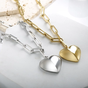 Polished gold and silver heart pendant necklaces with paperclip chains on stone base