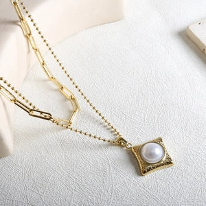 Détail d'un collier à deux rangs doré avec pendentif carré orné d'une perle blanche