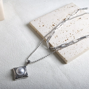Détail du collier argenté multicouche avec pendentif carré martelé et perle blanche