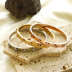 Stack of gold silver and rose gold star bracelets with crystals on a stone surface