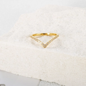 Macro detail of V-shaped gold ring featuring micro-pave crystals on a stone surface