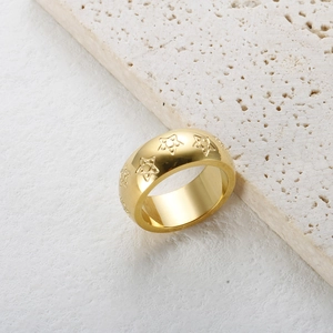 Primer plano de un anillo ancho dorado con estrellas en relieve sobre fondo de piedra