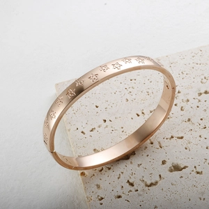 Elegante brazalete de oro rosa con estrellas grabadas sobre base de piedra travertino