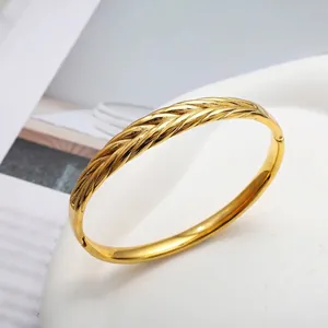 Golden olive leaf cuff bracelet with woven wheat texture on a white tray