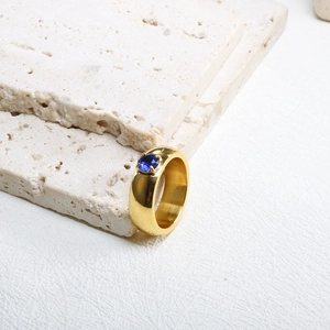 Détail d'une bague large en titane plaqué or ornée d'une pierre bleue sertie à griffes