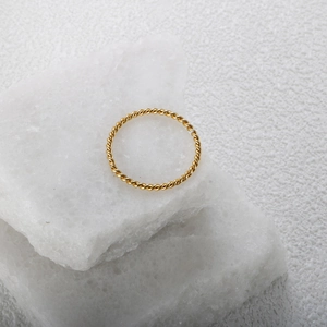 Minimalistischer 18K vergoldeter gedrehter Seilring auf weißem Steinhintergrund