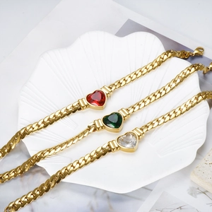 Detailed view of three gold Cuban link bracelets with emerald, ruby, and diamond heart crystals