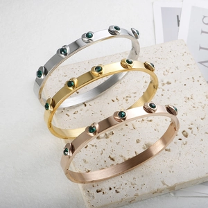 Detailed macro view of heart-shaped charms with green crystals on three metal bracelets