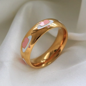 Vista macro di un anello dorato con cuore smaltato rosa e stella su seta bianca