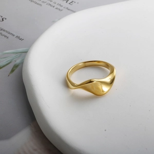 Minimalist 18k gold plated stainless steel ring with twisted wave pattern on white plate