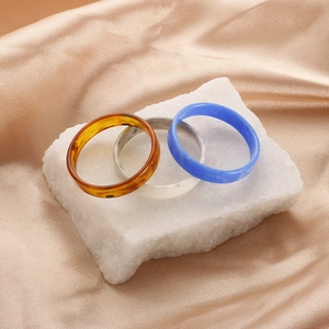 Detailed view of three resin stackable rings in amber, marble white and blue on a stone base