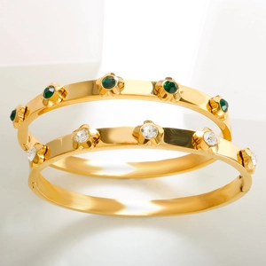 Detail of gold stainless steel bangle with floral engravings and emerald green gemstone