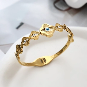 Makroaufnahme eines vergoldeten Evil Eye Armreifs mit Blumenmuster auf Keramik