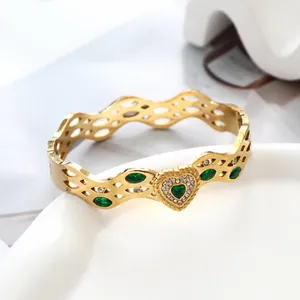Nahaufnahme vom goldenen Wellenarmband mit grünem Herzstein und weißen Zirkonia-Steinen