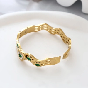Makroaufnahme des goldenen Wellenarmbands mit grünen Markisesteinen und Mikro-Pavé-Diamanten