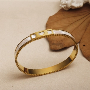 Detail of gold titanium bangle featuring white shell inlay and heart cutout accents