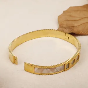 Detailed shot of gold titanium steel open bangle with white shell inlay and hollowed design