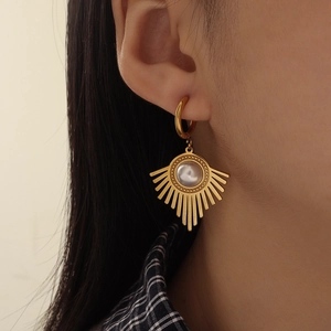 Close-up of gold U-shaped earring with white pearl and sunburst radial design