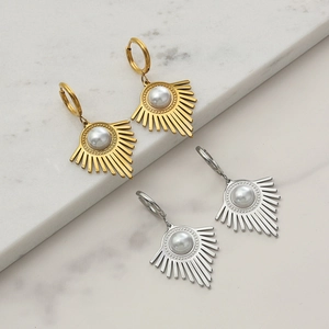 Close-up of gold and silver sunburst pendant earrings with pearls on marble stone