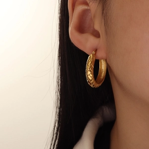Detail of 18K gold U-shaped earrings featuring a textured geometric cross-hatch pattern