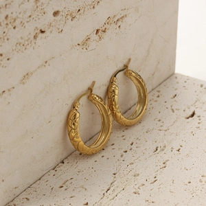 Detail of 18K gold-plated U-shaped earrings with embossed pattern on travertine stone
