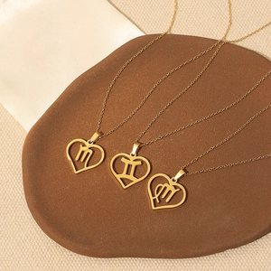 Three gold stainless steel heart zodiac necklaces displayed on a dark stone background