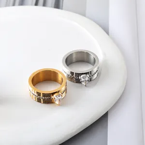Macro shot of gold and silver ribbed stainless steel rings with pear-cut zircon on white ceramic
