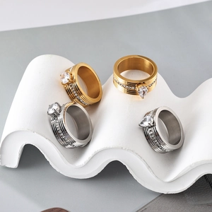 Close-up of wide stainless steel rings with large center stones on a wavy display