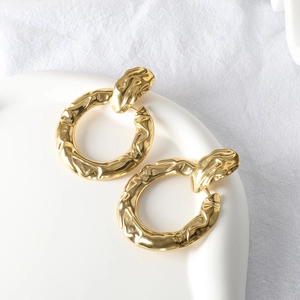 Close-up of golden irregular textured earrings with molten lava effect on a white tray