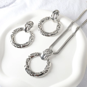Detail of silver jewelry set with crinkled texture on a white ceramic plate