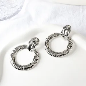 Macro detail of silver textured hoop earrings with hammered metal finish on white ceramic