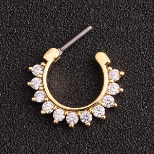 Hinged gold septum ring with eleven clear round zircons on a textured black surface